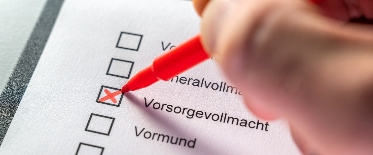 Jemand setzt ein Kreuz auf einem Papier, neben Vorsorgevollmacht