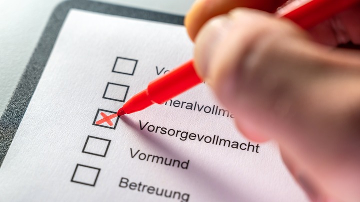 Jemand setzt ein Kreuz auf einem Papier, neben Vorsorgevollmacht